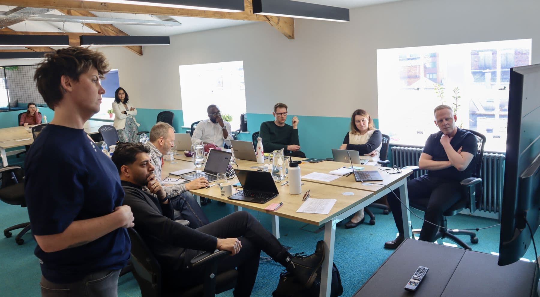A team workshop: people around tables with laptops in a bright office