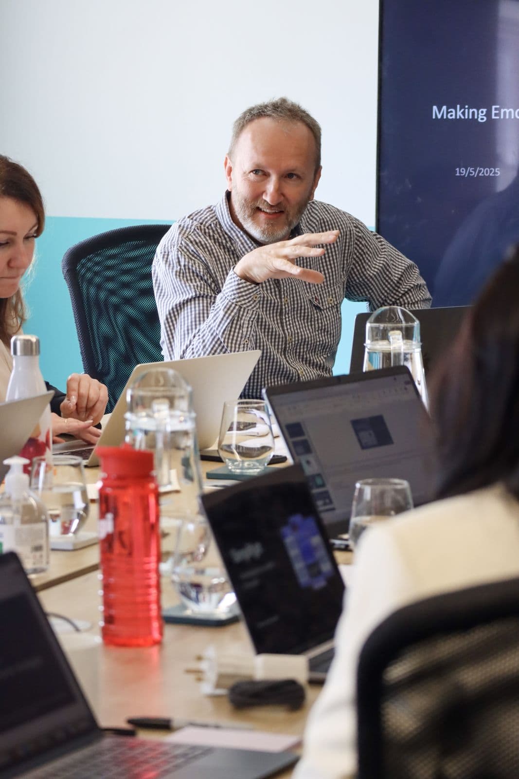 Jonathan Prescott mid-conversation at a meeting table surrounded by laptops