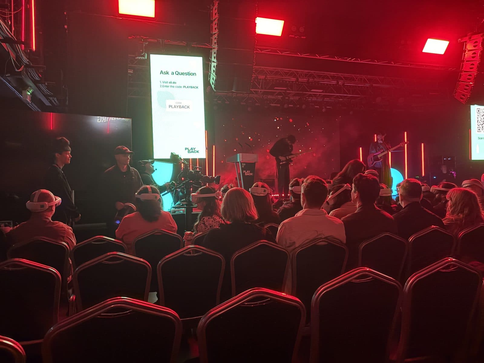 Audience in VR headsets facing the PLAYBACK main stage at Tramshed, Cardiff, with a band performing and a PLAYBACK lectern